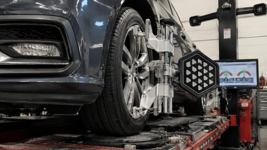 Close-up of a car's front wheel undergoing precision wheel alignment in Simon's Auto Repair, with alignment sensors attached and a monitor showing alignment readings.
